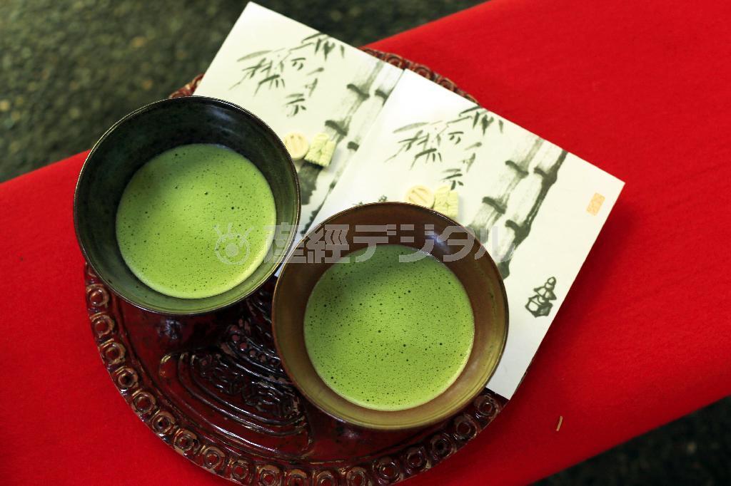 緑色の抹茶を引き立てるには、赤をバックにした方が緑が強調されると思い、茶碗（ちゃわん）をいすに敷かれた毛氈（もうせん）の上に置いて撮影しました。抹茶の泡が消えないうちに撮影を素早く済ませておいしい温度でいただきたいところですが、いくつかパターンを変えて撮影してみましょう。縦、横、広角で人が入っているカットと４カットを２分以内に撮影しました＝２０１５年４月２９日、神奈川県鎌倉市（須藤夕子さん撮影）