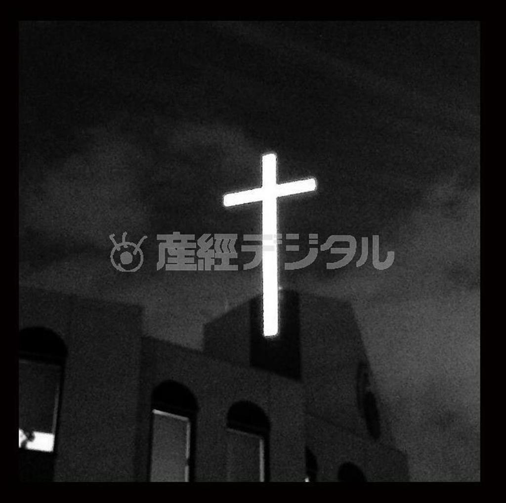 写真編集でモノクロ表現に変更した。薄暮の中、赤い光に包まれた、教会の十字架が浮かび上がっていた。カラーでも十分に奇麗だったがあえてモノクロに仕上げる方がより絵画的な雰囲気が出ると思ったのだ＝２０１４年１１月１９日、ｉＰｈｏｎｅ５ｓで（野口隆史さん撮影）