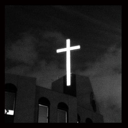 写真編集でモノクロ表現に変更した。薄暮の中、赤い光に包まれた、教会の十字架が浮かび上がっていた。カラーでも十分に奇麗だったがあえてモノクロに仕上げる方がより絵画的な雰囲気が出ると思ったのだ＝２０１４年１１月１９日、ｉＰｈｏｎｅ５ｓで（野口隆史さん撮影）