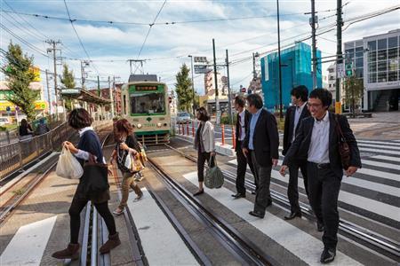 路面電車である都電荒川線の駅で、車両の前を笑顔で横切る歩行者。愛さずにはいられない電車の一つだ＝２０１２年１０月１２日、東京都荒川区（デイモン・コーターさん撮影）