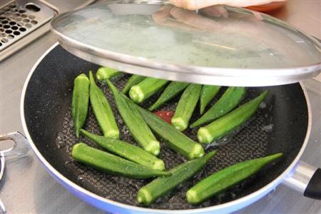 オクラとイカのピリ辛炒め（作り方１）＿＿サラダ油の半量を熱し、オクラを炒める。塩をふって水を回し入れ、蓋をして蒸し煮にする。ざるにあけ、水けをきる。