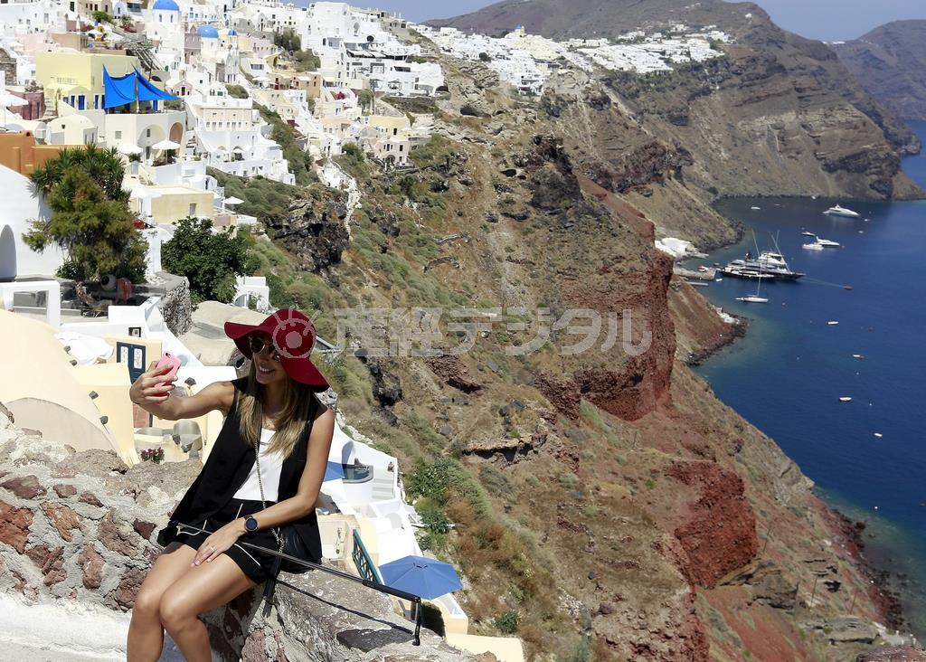 ギリシャのエーゲ海に浮かぶサントリーニ島で、断崖絶壁を背にセルフィーを撮る観光客。ただ、旅の思い出を大切に守りたいのなら、危険な位置取りでの撮影はなるべく控えた方が無難だ＝２０１５年７月１日（ロイター）