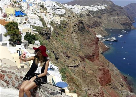 ギリシャのエーゲ海に浮かぶサントリーニ島で、断崖絶壁を背にセルフィーを撮る観光客。ただ、旅の思い出を大切に守りたいのなら、危険な位置取りでの撮影はなるべく控えた方が無難だ＝２０１５年７月１日（ロイター）