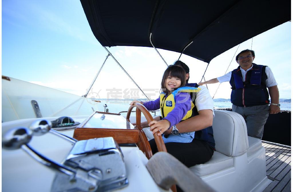 逗子マリーナのクルージングツアーに参加しました。子供を運転席に乗せてくれ、スタッフの方が優しく指導してくれました。上機嫌な笑顔をまず撮りたいのと、ここがどこで何をしているのか？を１枚に収めるには、やはり広角のレンズを選ぶとよいでしょう。船の上は揺れているので、シャッタースピードはなるべく早めにしてブレないように、自分の体をどこかに固定させましょう＝２０１５年６月７日、神奈川県逗子市（須藤夕子さん撮影）