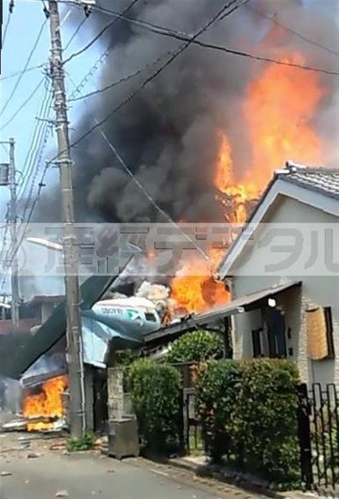 墜落し炎を上げる小型機と住宅。電柱の後ろに尾翼が見えている＝２０１５年７月２６日午前、東京都調布市（目撃者の動画より、提供写真）