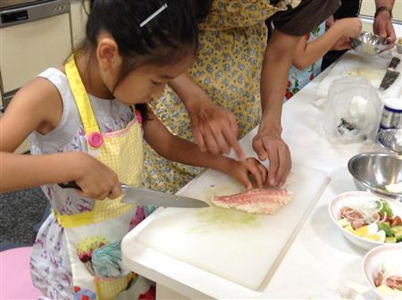 母親に教わりながら、慣れない手つきで「愛鯛」の切り身に包丁を入れる女の子＝２０１５年８月９日（日本財団撮影）