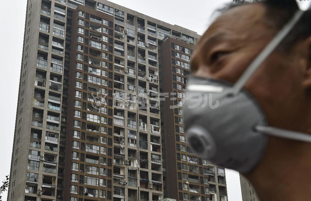 爆風で窓ガラスが破壊されたマンション前で、途方に暮れるマスク姿の住民＝２０１５年８月１９日、中国・天津市（共同）