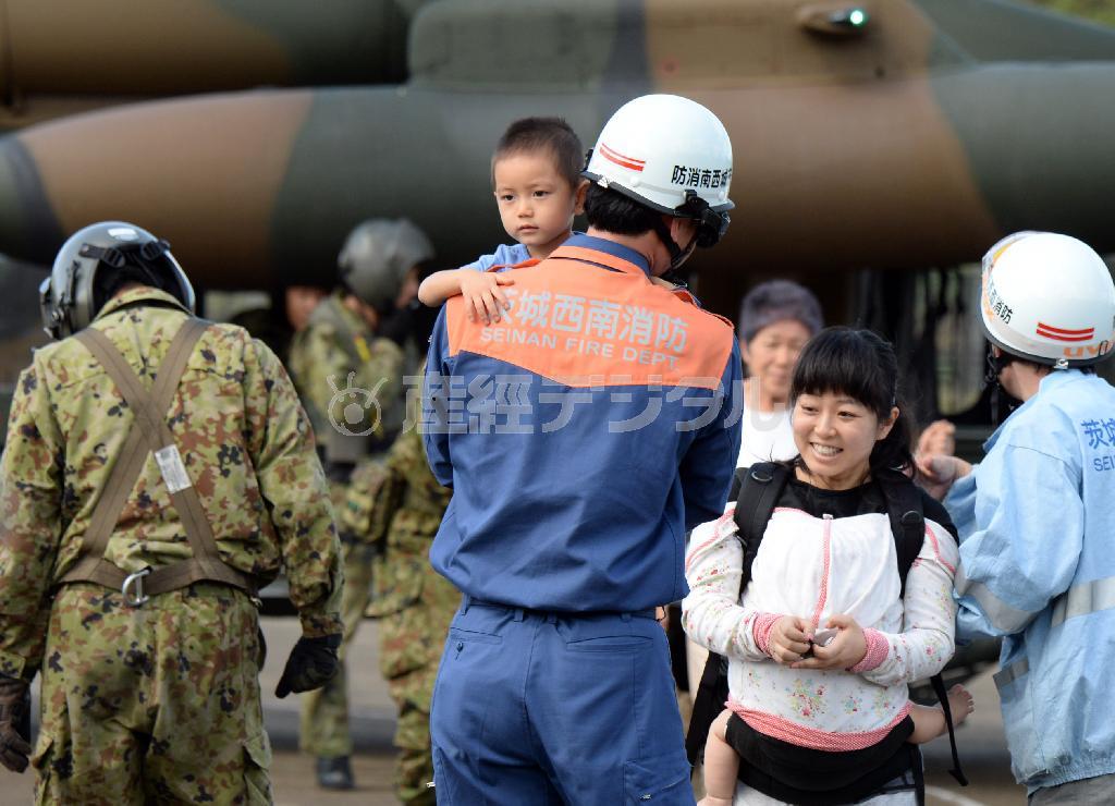孤立した住宅などで一夜を明かし、自衛隊のヘリコプターで救助され、消防隊員に抱きかかえられる子供と、幼児を抱き、笑顔を見せる女性＝２０１５年９月１１日午前、茨城県常総市（川口良介撮影）
