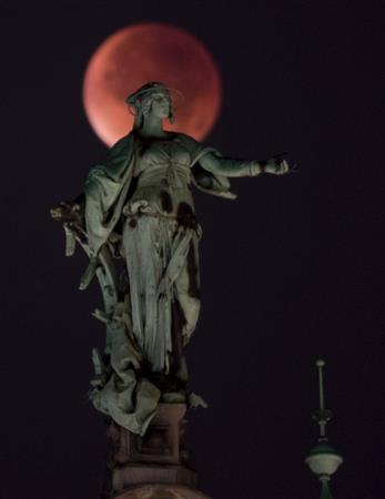 赤銅色に染まったスーパームーンが、皆既月食によって次第に欠けていく様子が観察され、ハンブルグ市庁舎の銅像を背景に幻想的な月が浮かび上がった＝２０１５年９月２８日、ドイツ・ハンブルク（ロイター）