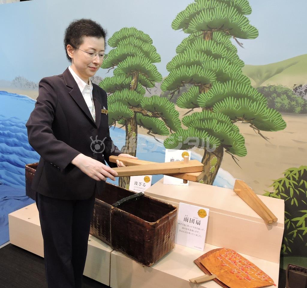 船を漕ぐ「櫓」の音を出す木を持つ、歌舞伎座ギャラリーの田野暦室長。波の音を出す「波ざる」（左下）には小豆が入っており、左右に動かして使う。雨音を出す「雨団扇」（右下）にはビーズがたこ糸で付けられ、扇ぎ方の強弱で強い雨、弱い雨と音を使い分ける＝２０１５年９月１１日、東京都中央区銀座（藤沢志穂子撮影）