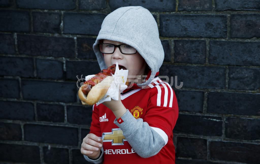 大きな口を開けて、ホットドッグにかぶりつく少年。世界保健機関（ＷＨＯ）の研究機関がソーセージなどの加工肉に高い発がん性が認められると発表し衝撃が広がっている＝２０１５年９月３０日、英国・マンチェスター（ロイター）