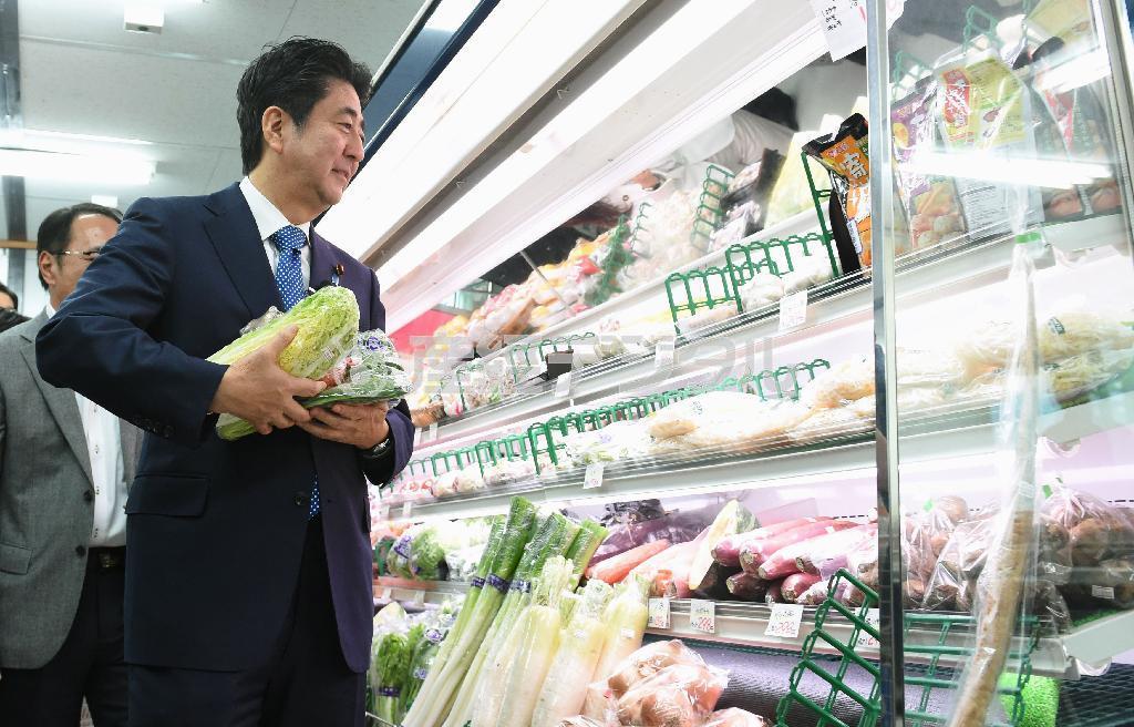 軽減税率では、生鮮食料品の扱いも焦点の一つ。１０月１９日、福島県双葉郡楢葉町の仮説商店街で野菜を買う安倍晋三（しんぞう）首相＝２０１５年（代表撮影）