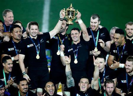 史上初の連覇を果たしたニュージーランドのフィフティーンに囲まれ優勝カップを掲げるニュージーランドの主将、リッチー・マコウ（左）とダニエル・カーター＝２０１５年１０月３１日、英国・首都ロンドン郊外のトゥイッケナム競技場（ＡＰ）