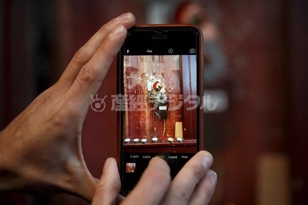テロの生々しさを伝えるカフェの窓に残る弾痕や花をスマホで撮影する人。こうした画像や動画がＳＮＳを通じて瞬く間に世界に広がった＝２０１５年１１月１５日、フランス・首都パリ（ＡＰ）