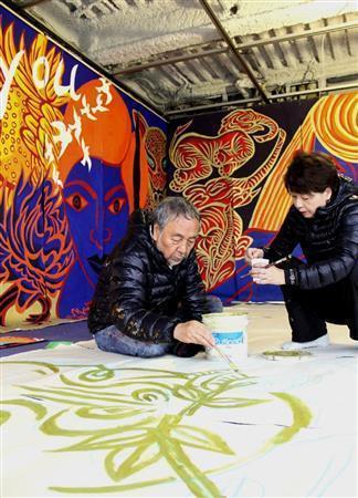 １組が長さ９．４メートル、高さ３メートルの巨大な帆布に絵を描くキーヤン。金で縁取りをしてアクリル絵の具で完成させる。右は、制作チームのメンバーでもある妻の知位子さん＝２０１５年４月１４日、京都市中京区のキーヤンスタジオ（田中幸美撮影）