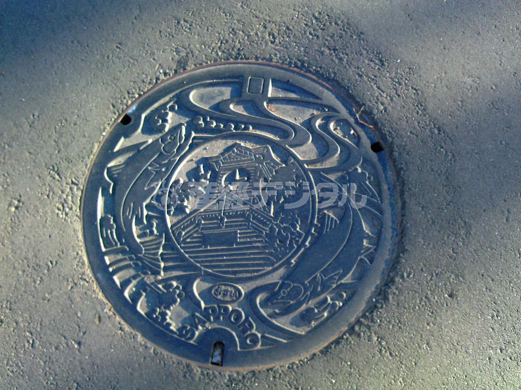 時計台と鮭があしらわれた札幌ご当地デザインのマンホール。ついに２０センチほど積雪したので、見えなくなってしまいました＝２０１５年９月１６日、北海道札幌市（乾ルカさん撮影）