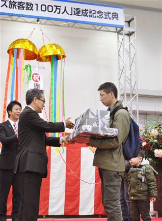 クルーズ船で訪日した外国人が年間１００万人に達し、江島潔国交政務官（左）から記念品を受け取る中国から来た家族＝８日午前、福岡市の博多港