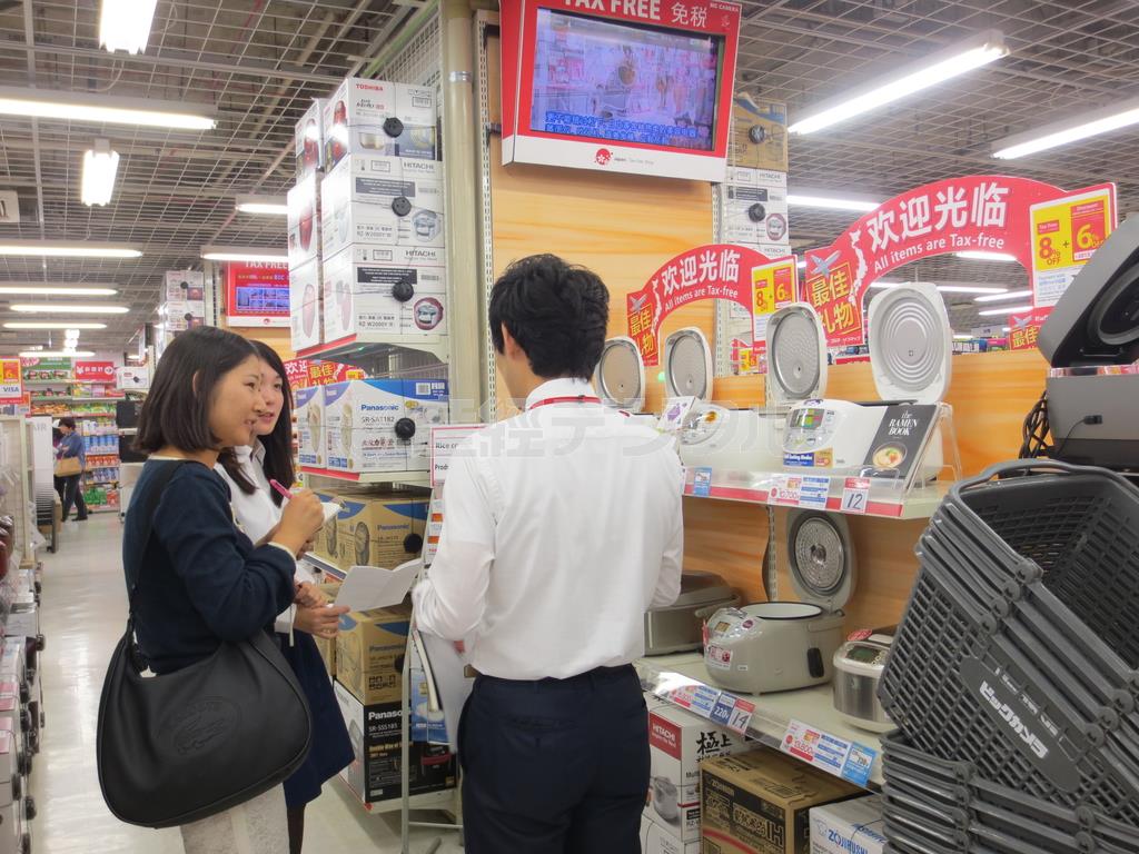 訪日外国人客向けの免税商品が並ぶビックカメラ有楽町店の３階フロアで担当者（右）に取材をする学生記者＝２０１５（平成２７）年１１月４日、東京都千代田区（昭和女子大学、有志学生記者撮影）
