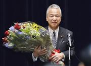 退任のあいさつを終え、職員から受け取った花束を手にする甘利前経済再生相＝２９日午前、内閣府