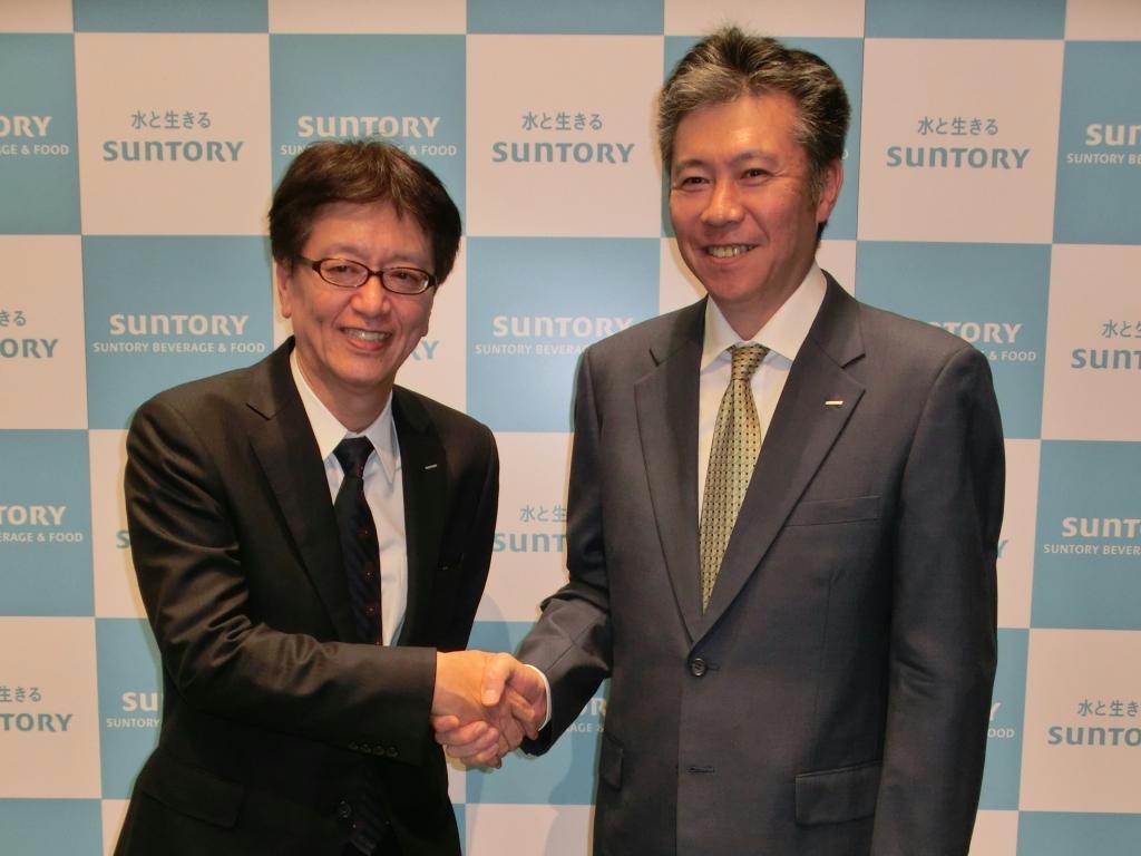 サントリー食品インターナショナルの鳥井信宏社長（右）と握手する小郷三朗副社長＝１２日、東京都中央区