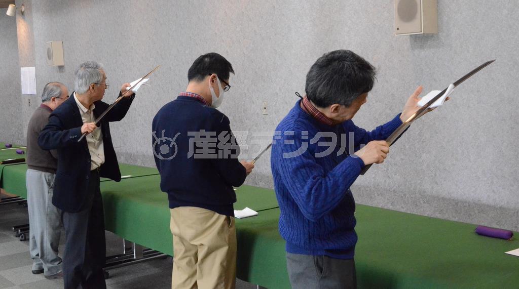 【定例鑑賞会】参加してくるベテランたちは、さすがに刀の扱い方は手慣れたものだ。光源の方に刃先を向けて、浮かび上がる微妙な地肌や刃文の違いを見極める＝２０１６年２月１３日、東京都渋谷区（原圭介撮影）