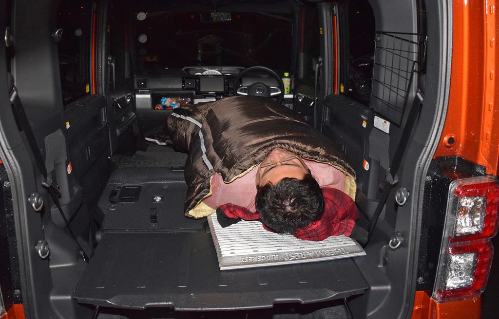 寝袋に収まる杉渕。写真のように、下半身をクルマの真ん中よりしてに寝ると、シートの段差を感じにくいそうだ。そうなると、大人２人が並んで寝るスペースはない