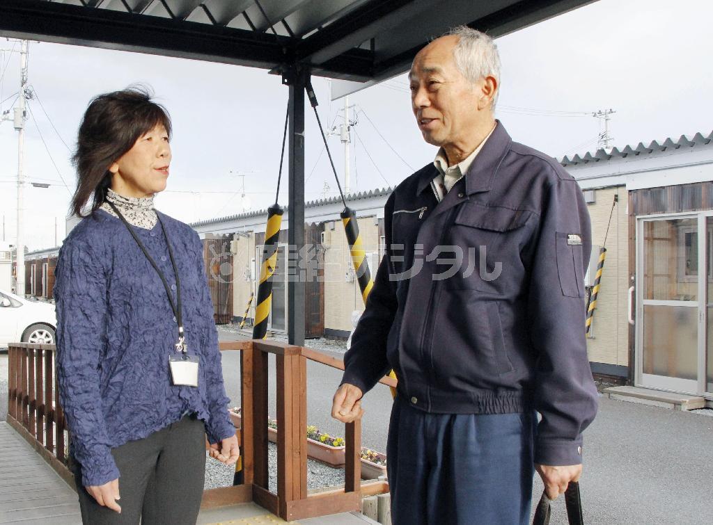 仮設住宅を訪れるＮＰＯ職員の女性と立ち話する飯崎行政区の杉重博区長（右）＝２０１６年３月２日、福島県南相馬市（共同）
