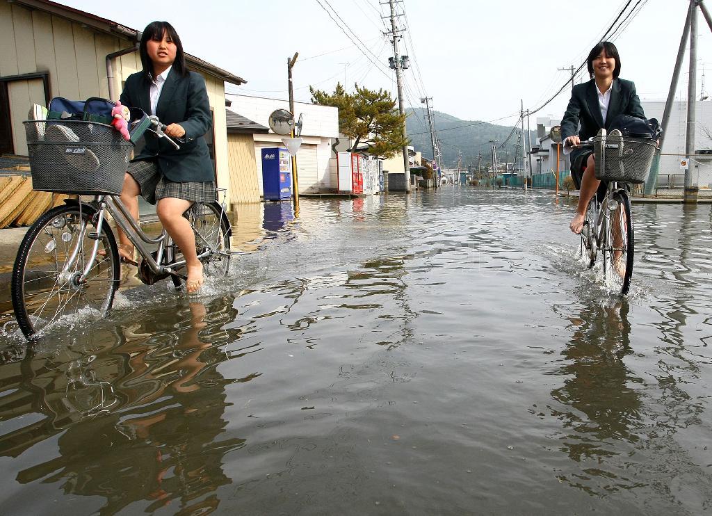 冠水した道路を裸足になって自転車に乗り下校する福島レイさん（左）＝２０１１年５月３１日、宮城県石巻市（桐山弘太撮影）