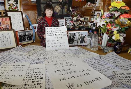 東日本大震災の津波で行方不明になった夫を思って記したメッセージと熊谷幸子さん。仏壇の周りには、死亡届を出していない夫の写真が並ぶ＝２０１５年１２月１７日、岩手県陸前高田市（共同）