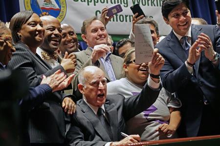 最低賃金の引き上げに署名したブラウン・カリフォルニア州知事（中央手前）＝４月４日、ロサンゼルス（ＡＰ）