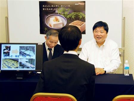 合同企業説明会で参加者（手前）に事業について話す、やまみの山名清社長（右）＝３月下旬、東京・渋谷