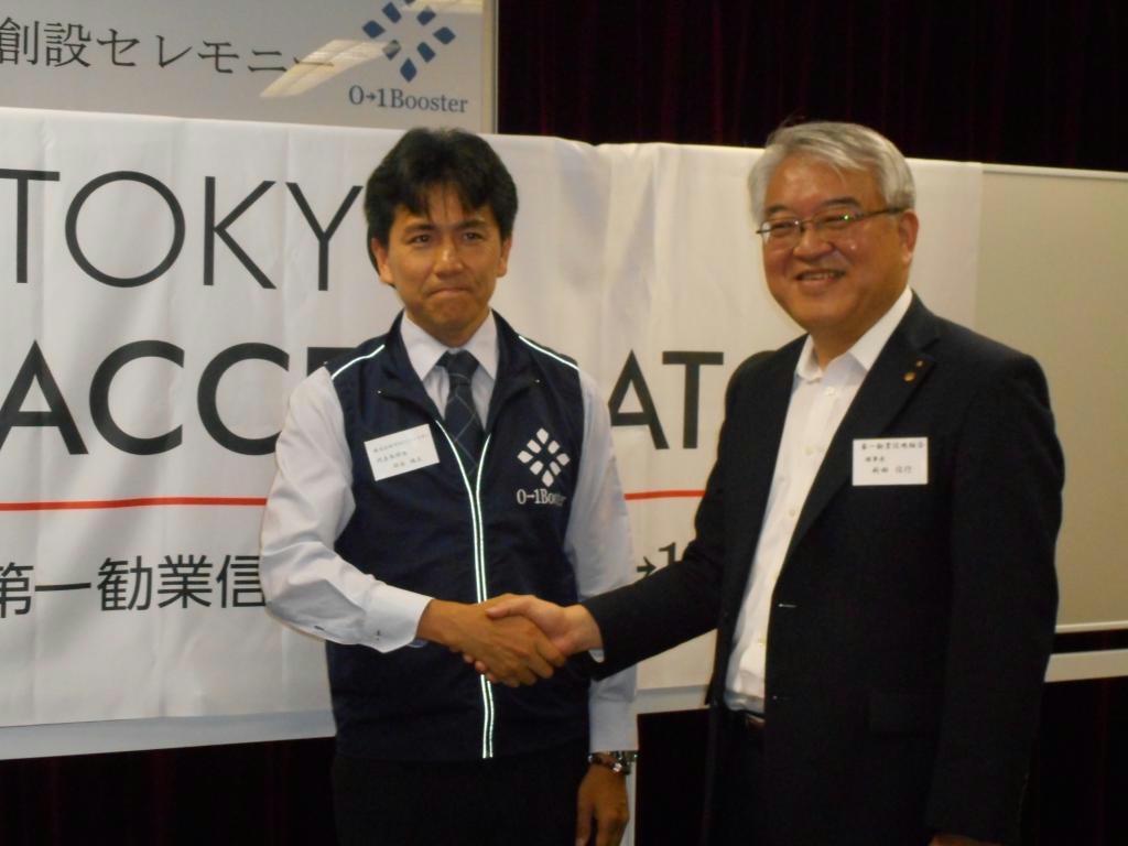 「東京アクセラレーター」で提携したゼロワンブースターの鈴木規文社長（左）と握手する新田信行・第一勧業信用組合理事長＝５月１８日、東京都新宿区