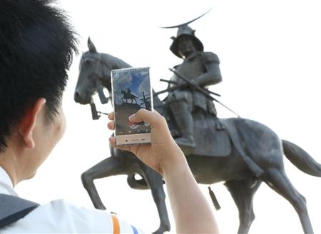仙台市で伊達政宗像にスマートフォンを向け、「ポケモンＧＯ」のキャラクターを探す人＝２２日午後