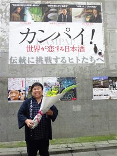 映画「カンパイ！世界が恋する日本酒」の看板の前に立つ、南部美人の久慈社長