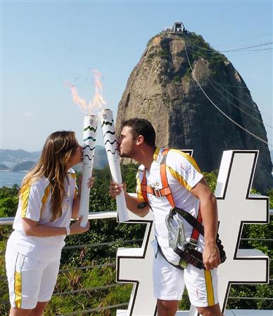 リオ五輪開幕を目前に控え、聖火リレーで聖火を引き継ぐランナー。後方は有名観光地「ポン・ジ・アスーカル」＝５日、リオデジャネイロ（共同）