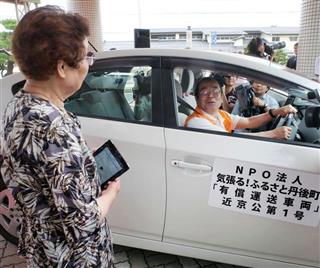 ウーバーのシステムを活用した京丹後市の「ささえ合い交通」。手にしたタブレット端末のアプリで女性が配車を依頼すると、自家用車が到着した。こうした取り組みを広げることができるか＝５月、京都府京丹後市