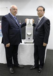 臨床試験で使われたイオン発生装置を披露するシャープの沖津雅浩常務（右）とジョージア国立結核病院のザザ・アヴァリアニ院長＝８日、東京都港区