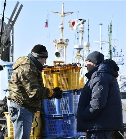 北方領土周辺海域で採れたウニを北海道根室市の花咲港で水揚げしたロシアの水産関係者。漁船のマストには日ロの国旗が並ぶ＝１６日午前