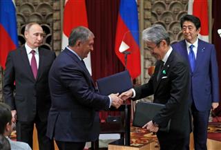 安倍晋三首相とプーチン大統領の立ち会いでロシア国営石油会社ロスネフチのセチン社長（中央左）と握手する丸紅の国分文也社長（同右）＝２０１６年１２月、東京都内（ＡＰ）