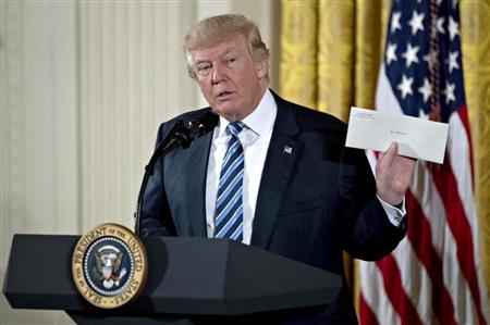２２日、ホワイトハウスでの高官の就任宣誓式で、オバマ前大統領が残した封筒を掲げるトランプ米大統領（ゲッティ＝共同）