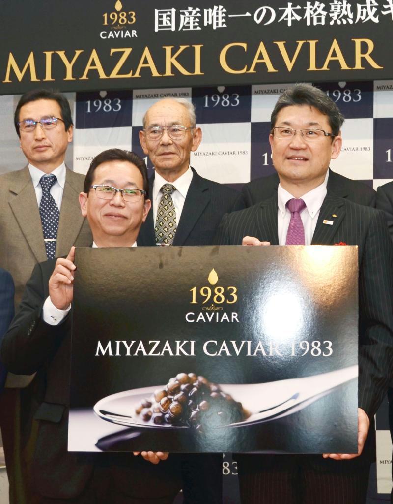 国産キャビアが初輸出された宮崎空港での記念式典で、パネルを手にするジャパンキャビアの坂元基雄社長（左）と河野俊嗣宮崎県知事（右）＝８日、宮崎市
