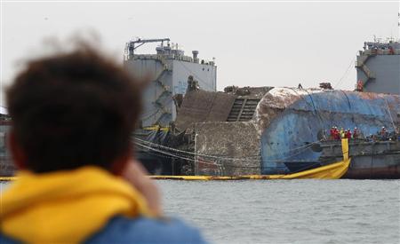 遺族（手前）が見守る中、引き揚げ作業で海面に浮上したセウォル号＝２４日、韓国南西部の珍島沖（代表撮影・共同）