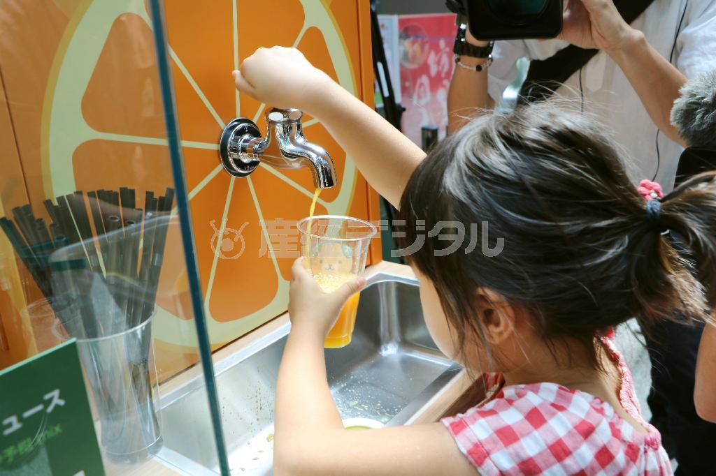 「みかん蛇口」からジュースをカップに注ぐ女の子＝２０日午前、松山空港