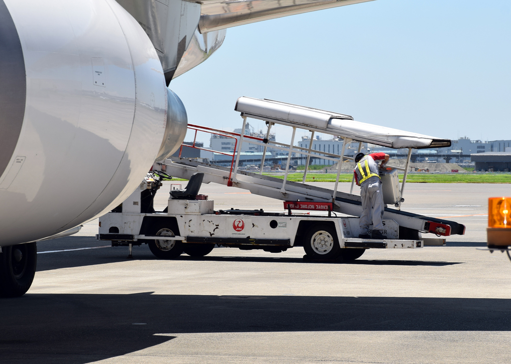 搭乗が遅れた乗客の手荷物をベルトローダーで積み込むグランドスタッフ