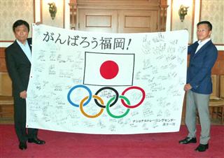 国内トップアスリートらが寄せ書きをした復興応援旗を披露する元レスリング男子日本代表の池松和彦さん（右）と小川洋福岡県知事＝２６日午前、福岡県庁