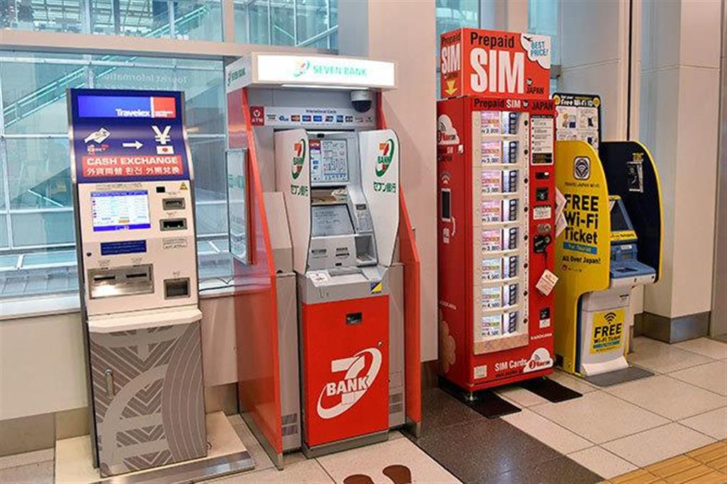 2016年6月13日、羽田空港の国際線到着ロビーに設置された、（左から）外貨両替機、セブン銀行のATM、プリペイドSIMの販売機、フリーWi－Fiのチケット販売機（東京都大田区）（写真＝時事通信フォト）