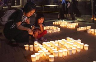 岡山県倉敷市真備町地区で「迎え火」のろうそくの灯を見つめる親子＝１３日夜