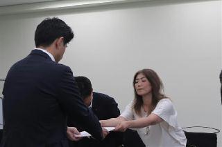 陳情書を手渡す田久保真紀さん。後ろ姿は資源エネルギー庁の山崎琢矢・新エネルギー課長＝２２日、東京都千代田区の経済産業省（三枝玄太郎撮影）