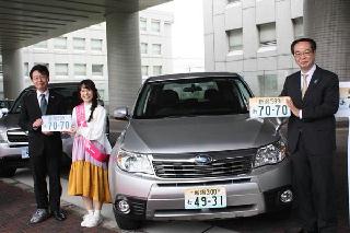 公用車の前で新潟版図柄入りナンバープレートをＰＲするＮａｏ☆さん（左から２人目）と、益田浩副知事（右端）、北陸信越運輸局の板崎龍介局長（左端）＝１１日、新潟市中央区の県庁前（太田泰撮影）