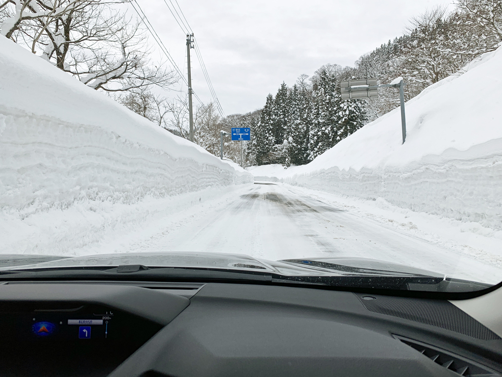 高い雪の壁に囲まれた圧雪路を進むフォレスター